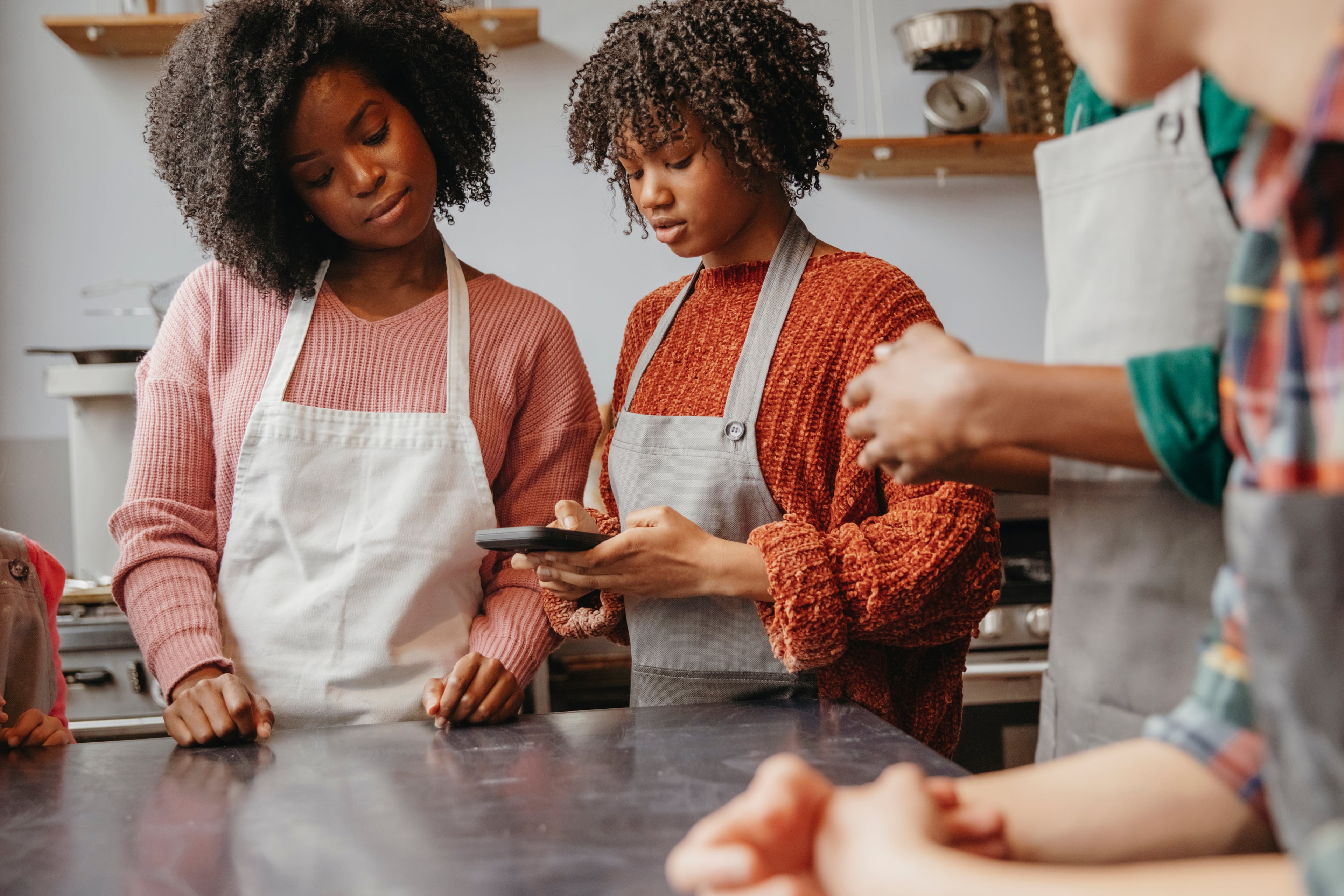 Two adults and a child in aprons looking at a smartphone in a kitchen.